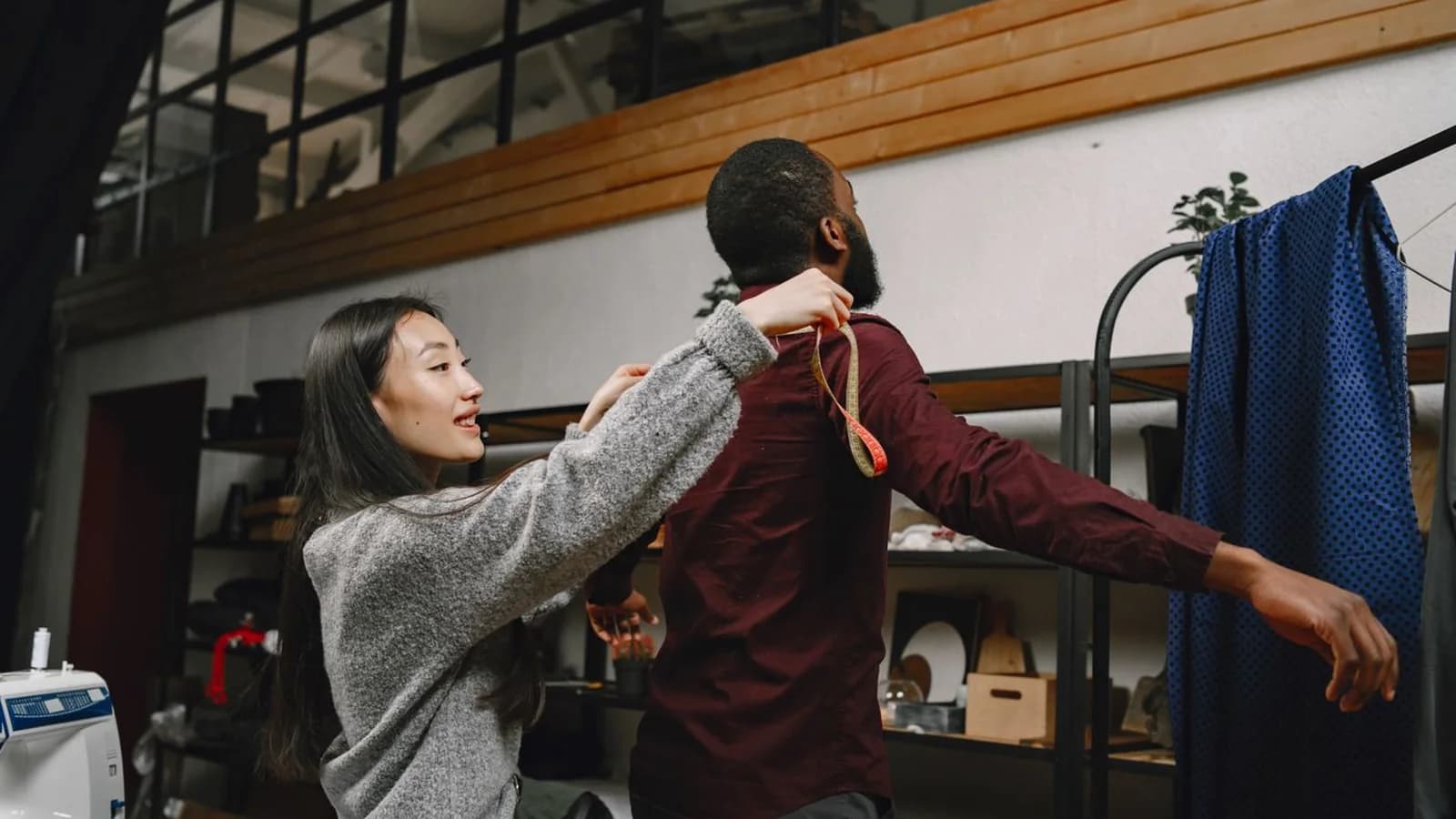 Tailor measuring the shoulder of a man wearing a burgundy shirt during a menswear fitting