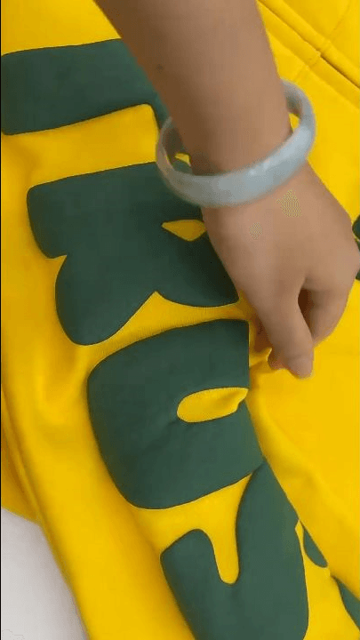 Hand checking large raised dark green print areas on a yellow garment