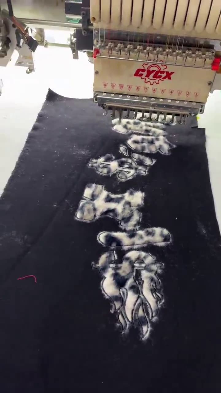 Embroidery machine head stitching a design onto black fabric at Meiting Garments