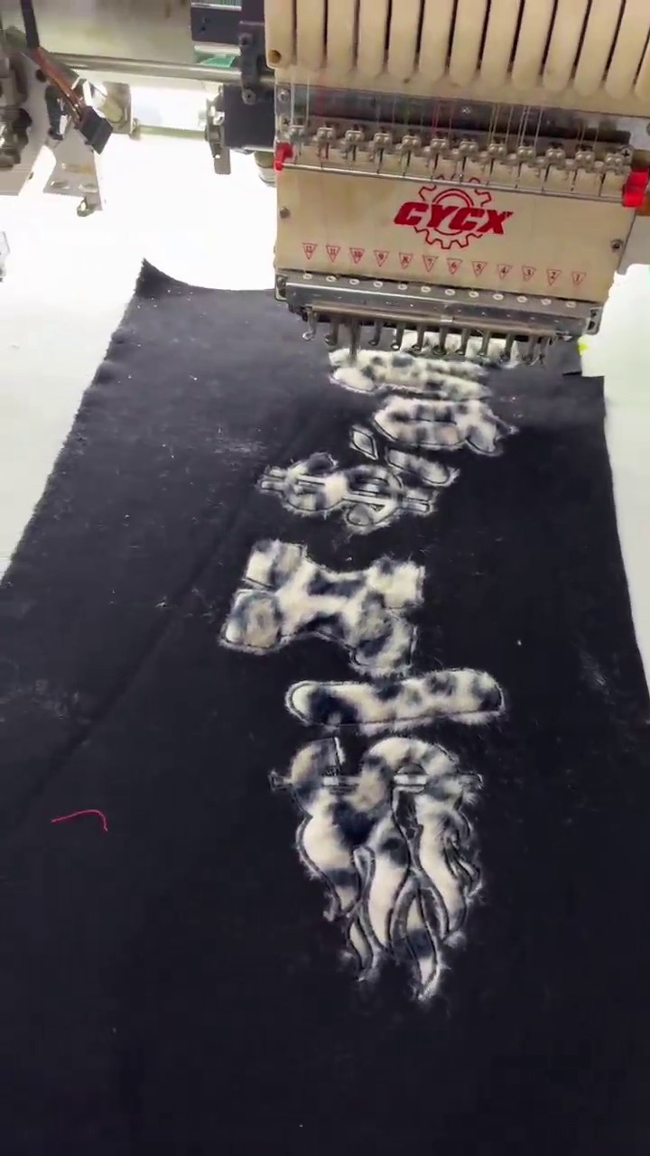 Embroidery machine head stitching a design onto black fabric at Meiting Garments